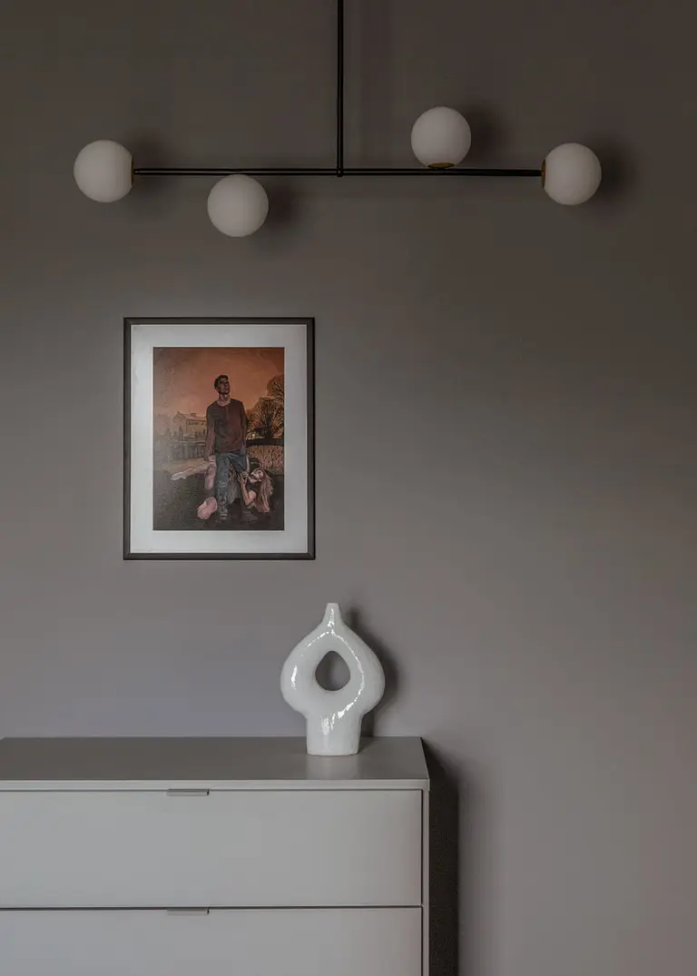Minimalistyczne wnętrze z szaro-białą komodą, nowoczesnym oświetleniem i obrazem.