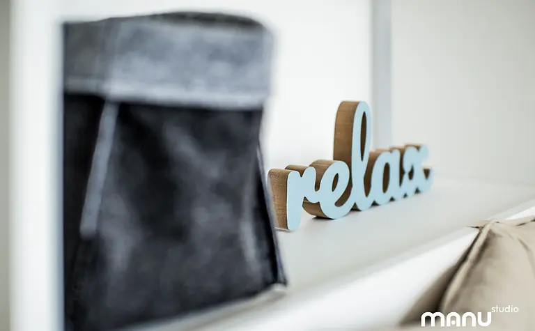 Nowoczesne wnętrze z minimalistycznym napisem relax oraz szarym pojemnikiem.