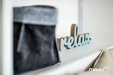 Nowoczesne wnętrze z minimalistycznym napisem relax oraz szarym pojemnikiem.