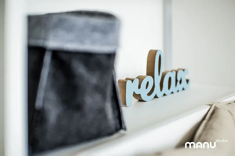 Nowoczesne wnętrze z minimalistycznym napisem relax oraz szarym pojemnikiem.