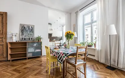 Wnętrze jadalni w stylu skandynawskim z kolorowym stołem, drewnianymi krzesłami i wazonem słoneczników.