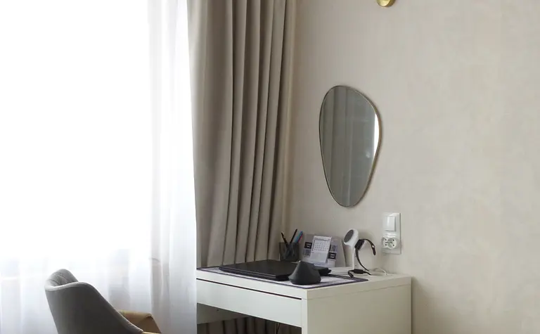 Minimalistyczny pokój z biurkiem, lustrem i jasnymi zasłonami.