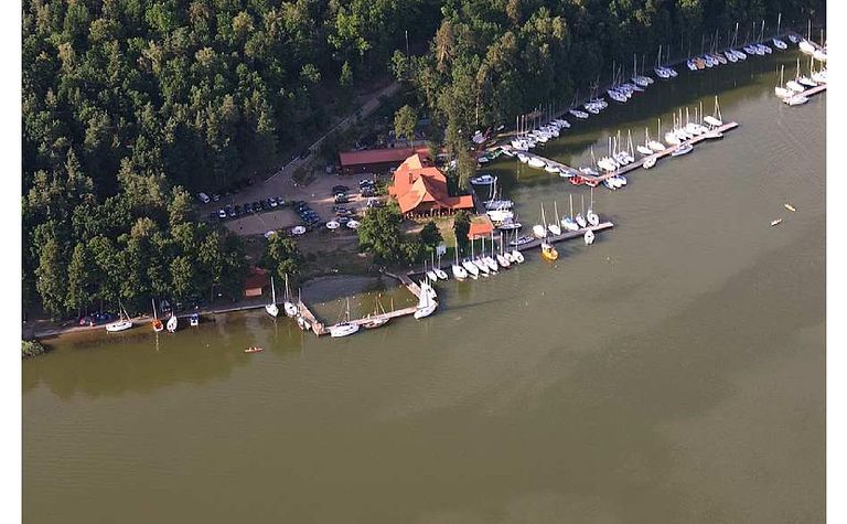 Widok portu z jachtami i drewnianym domkiem otoczonym zielenią. Minimalistyczny i nowoczesny styl.