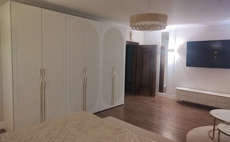 Sypialnia w stylu glamour z białymi meblami i drewnianą podłogą.