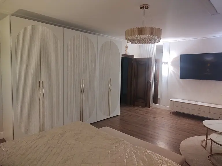 Sypialnia w stylu glamour z białymi meblami i drewnianą podłogą.