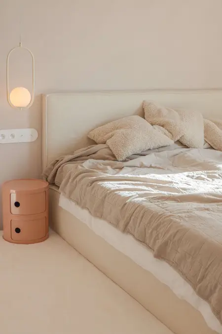 Sypialnia w stylu boho z beżowym łóżkiem, art deco lampą i eklektycznymi dodatkami.