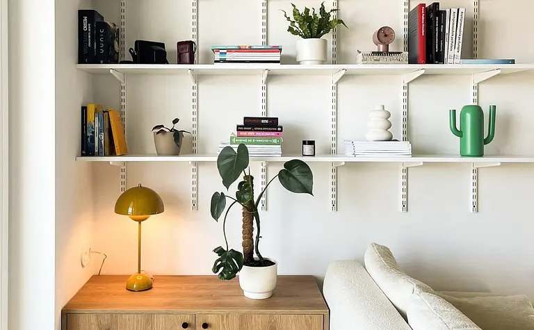 Minimalistyczny salon z drewnianą komodą, białą sofą i roślinami.