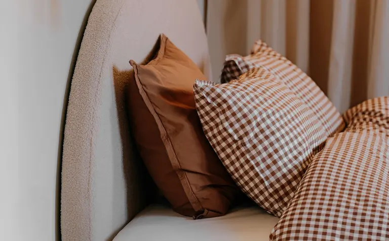 Sypialnia w stylu quiet luxury z beżowym łóżkiem i vintage poduszkami.