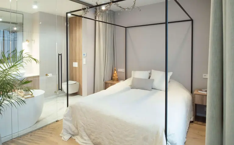 Sypialnia z łóżkiem, drewnianymi detalami i strefą łazienki w stylu quiet luxury.