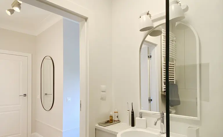 Nowoczesna łazienka z białą umywalką, lustrem i drewnianą podłogą, minimalistyczny design.