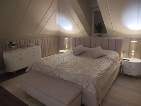 Sypialnia z jasnym łóżkiem, szafką i dekoracjami glamour.