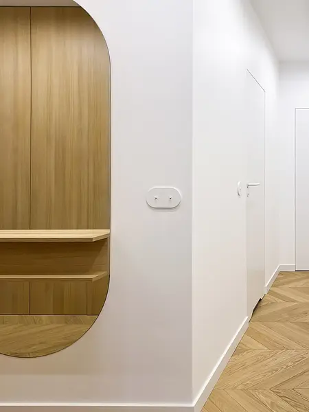 Minimalistyczny przedpokój z drewnianymi akcentami i białymi ścianami.