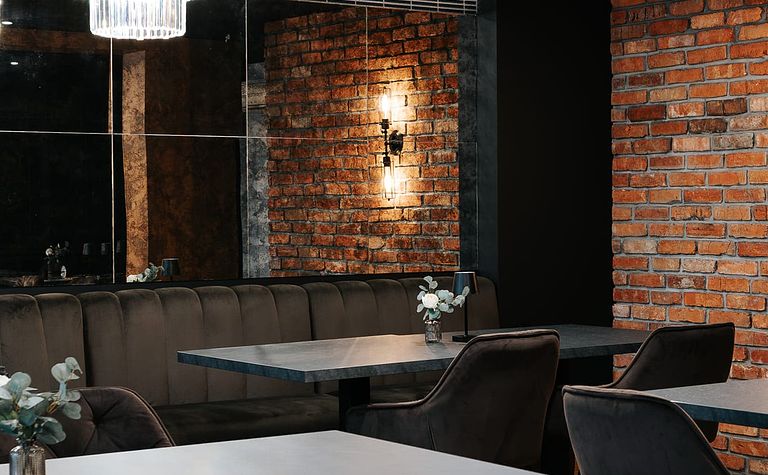 Wnętrze restauracji z ceglaną ścianą, eleganckimi meblami i industrialnym oświetleniem.