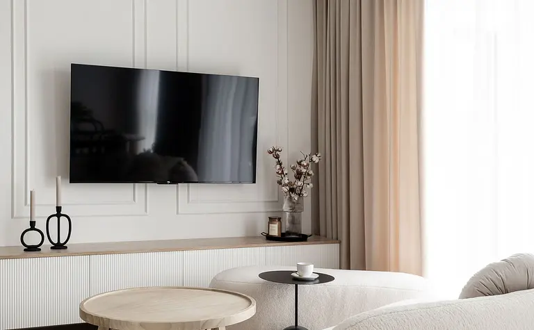 Współczesny salon z jasnymi meblami i telewizorem na ścianie.