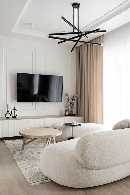 Współczesny salon z jasnymi meblami i telewizorem na ścianie.
