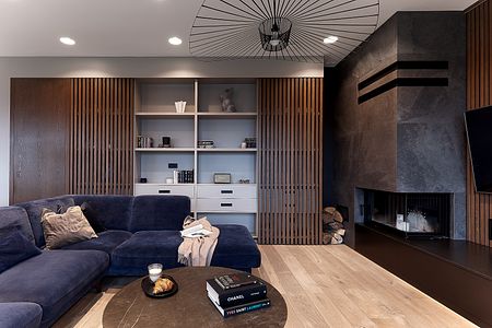 Wnętrze nowoczesnego salonu z niebieską kanapą, drewnianą półką i kominkiem.