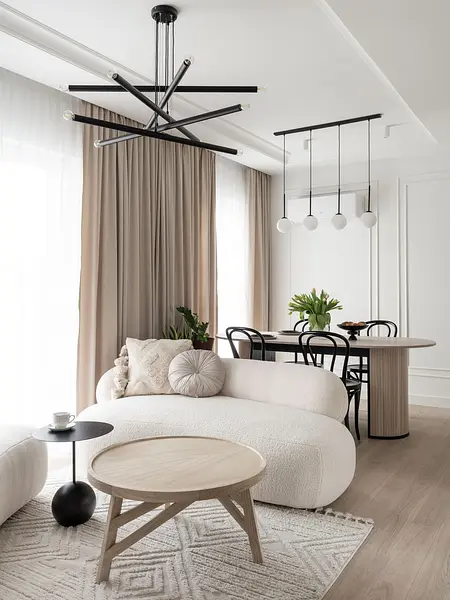 Współczesny salon z jasnymi meblami, drewnianym stołem i dekoracyjnymi roślinami.