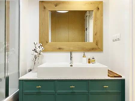 Nowoczesna łazienka z białą umywalką i drewnianym lustrem, minimalistyczny design.