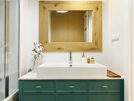 Nowoczesna łazienka z białą umywalką i drewnianym lustrem, minimalistyczny design.