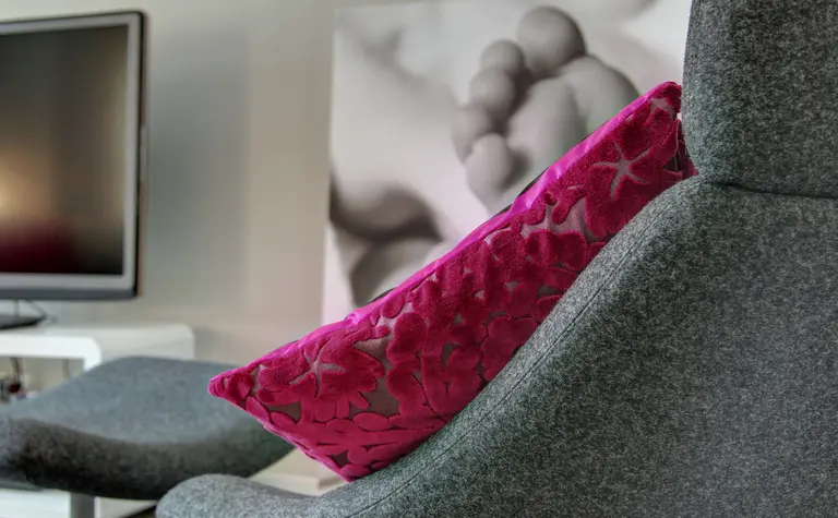 Wnętrze salonu z szarym fotelem i różową poduszką, minimalistyczny styl.