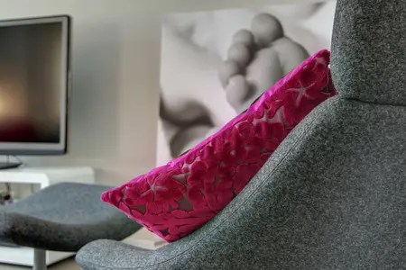 Wnętrze salonu z szarym fotelem i różową poduszką, minimalistyczny styl.