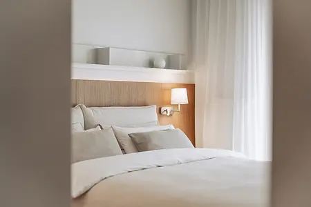 Sypialnia w stylu japandi z minimalistycznym wystrojem, białymi zasłonami i drewnianym łóżkiem.