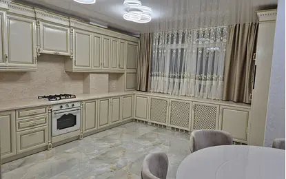 Kuchnia z jasnymi meblami, marmurową podłogą i zasłonami w stylu quiet luxury.