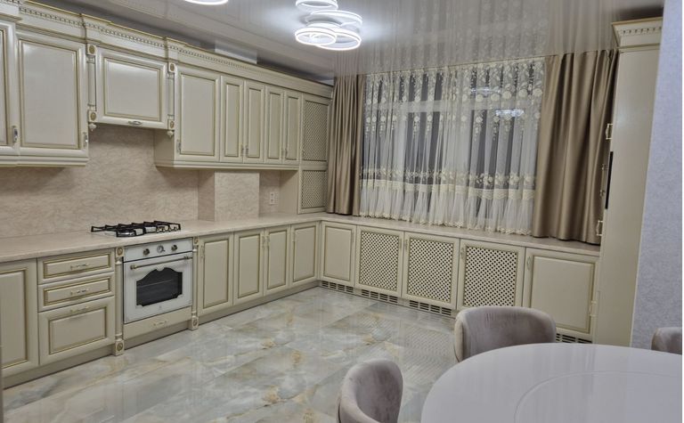 Kuchnia z jasnymi meblami, marmurową podłogą i zasłonami w stylu quiet luxury.