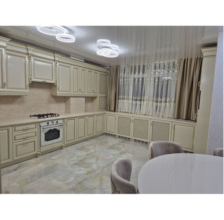 Kuchnia z jasnymi meblami, marmurową podłogą i zasłonami w stylu quiet luxury.