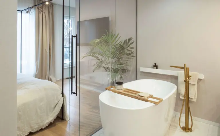 Nowoczesna łazienka z wolnostojącą wanną, drewnianymi detalami i roślinnością w stylu quiet luxury.
