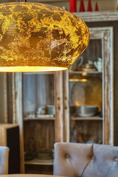 Stylowa jadalnia z elementami boho, vintage i rustykalnymi, złota lampa nad stołem.