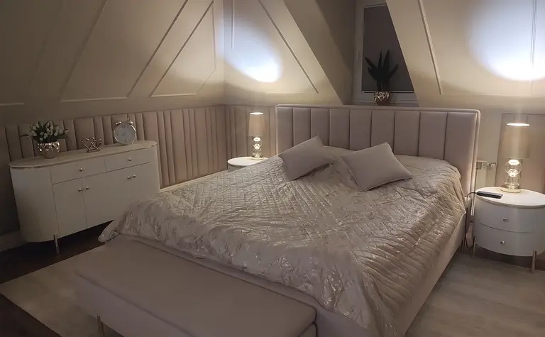 Sypialnia z jasnym łóżkiem, szafką i dekoracjami glamour.