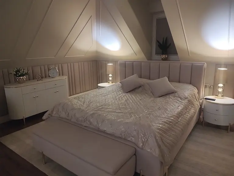 Sypialnia z jasnym łóżkiem, szafką i dekoracjami glamour.