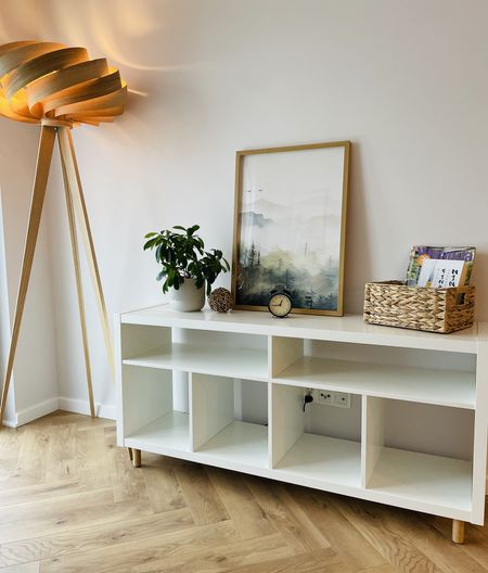 Minimalistyczne wnętrze z białym meblem, drewnianą lampą i rośliną