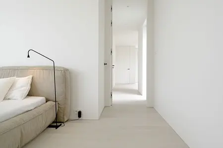 Wnętrze sypialni z minimalistycznym designem, jasnymi ścianami i beżowym łóżkiem.