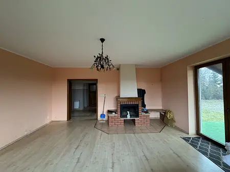 Wnętrze tradycyjnego salonu z kominkiem, drewnianą podłogą i dużymi oknami.