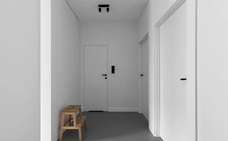 Przedpokój z minimalistycznym wystrojem, białe ściany i drewniana ławka.