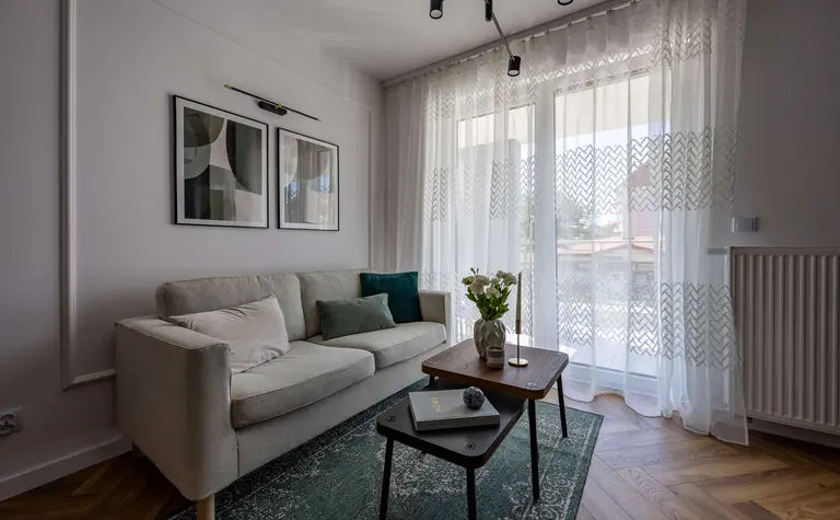 Współczesny salon z jasną sofą, zieloną wykładziną i drewnianymi akcentami.