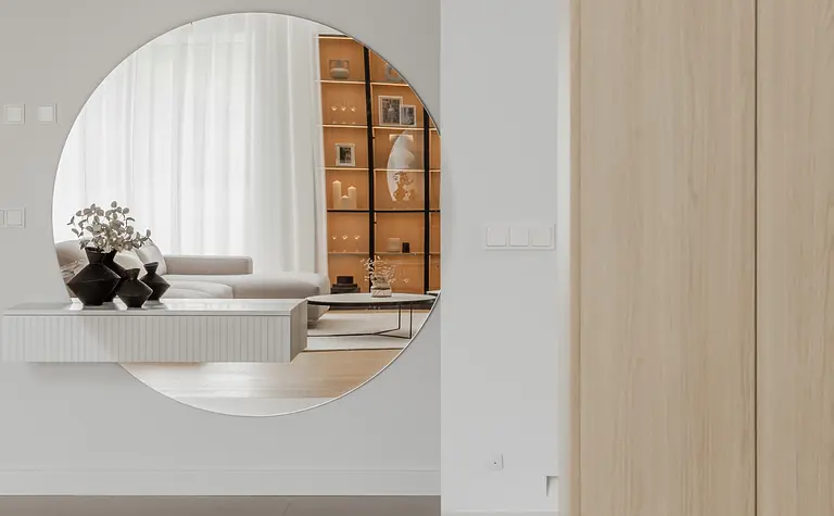 Wnętrze w stylu japandi z minimalistycznymi meblami i dużym lustrem okrągłym.