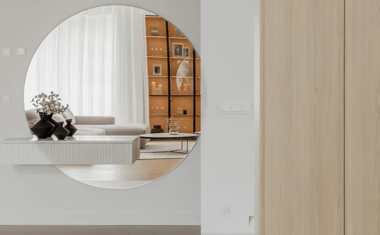 Wnętrze w stylu japandi z minimalistycznymi meblami i dużym lustrem okrągłym.