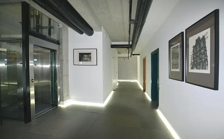 Współczesny korytarz z industrialnymi detalami i minimalistycznym oświetleniem.