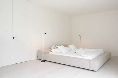 Sypialnia w stylu minimalistycznym z jasnym łóżkiem i białymi ścianami, elementy minimaluxe