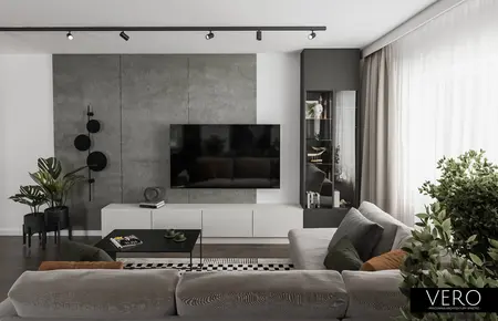 Minimalistyczny salon z zielonymi roślinami i szarymi meblami.