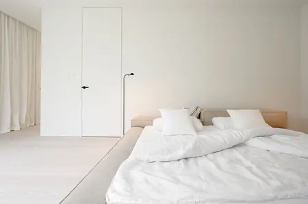Minimalistyczna sypialnia z białym łóżkiem, jasnymi zasłonami i nowoczesnymi detalami