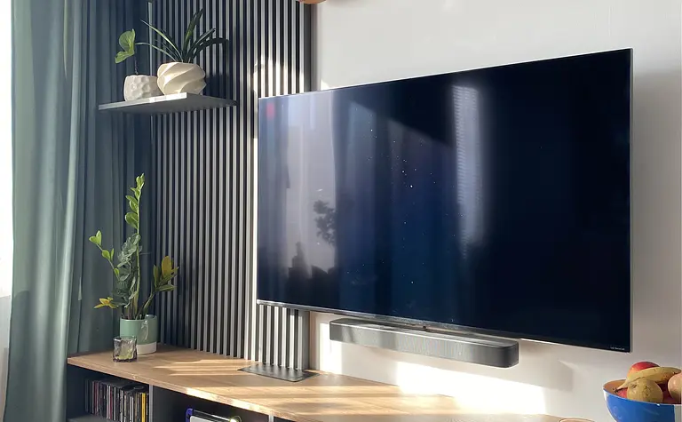 Nowoczesne wnętrze salonu z telewizorem, drewnianą półką i roślinami.