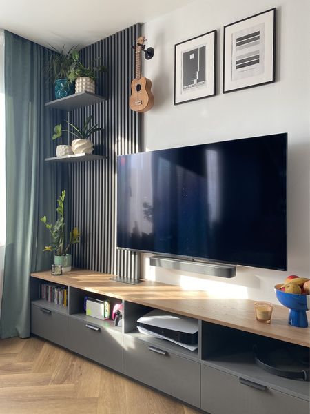 Nowoczesne wnętrze salonu z telewizorem, drewnianą półką i roślinami.