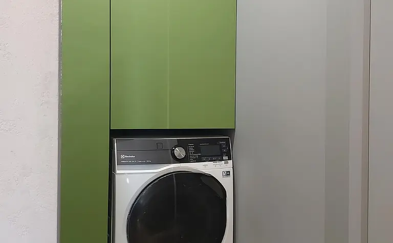 Pralnia w stylu industrialnym z zielonymi szafkami i nowoczesną pralką.