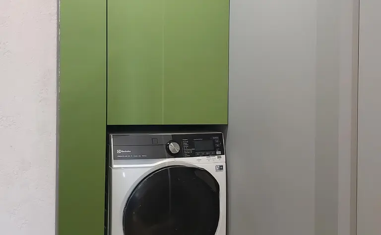 Pralnia w stylu industrialnym z zielonymi szafkami i nowoczesną pralką.