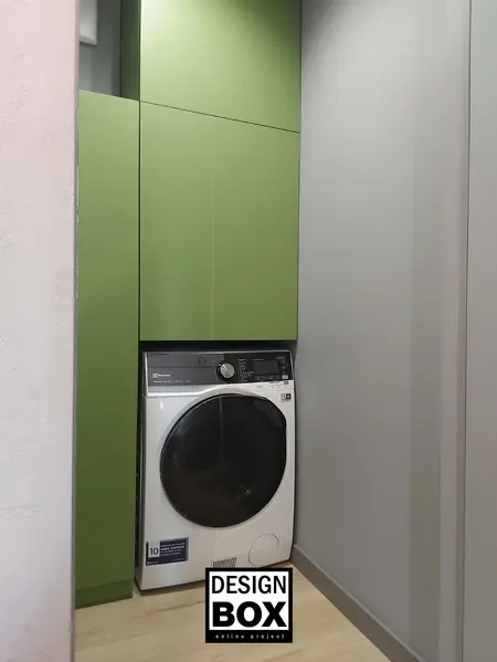 Pralnia w stylu industrialnym z zielonymi szafkami i nowoczesną pralką.