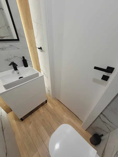 Minimalistyczna toaleta z białą umywalką i drewnianą podłogą, nowoczesne akcenty